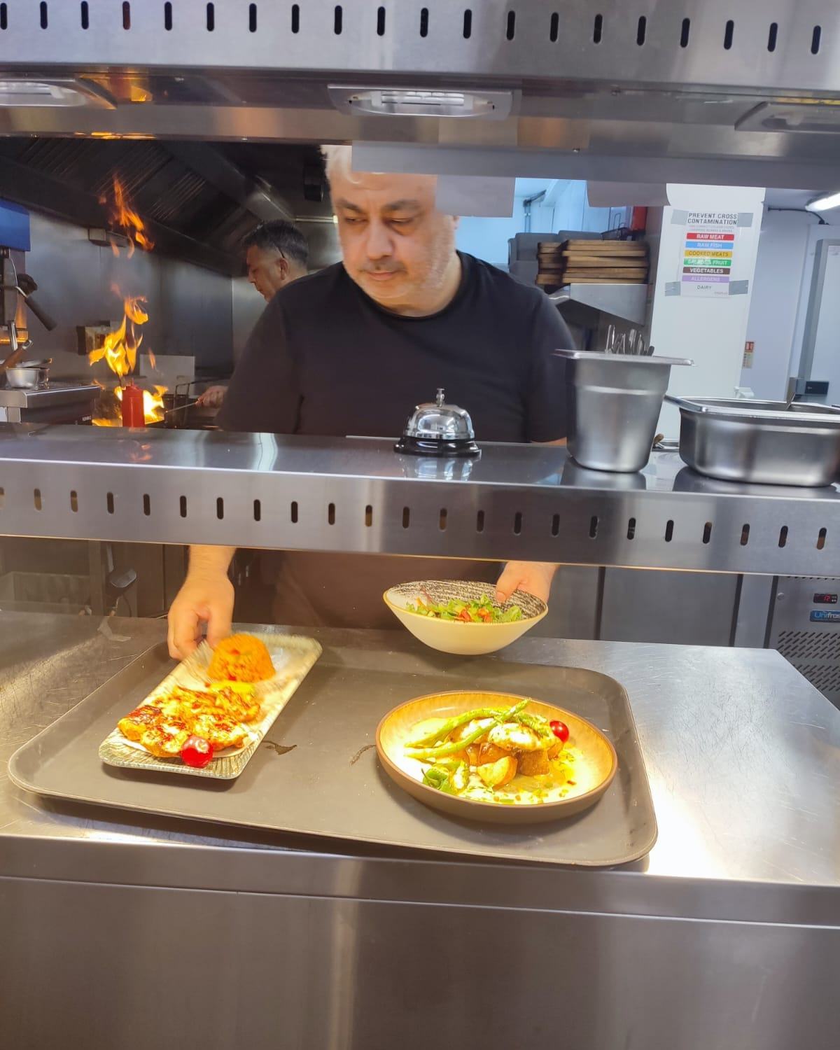 Haydar Sevincli plating dishes at the pass with flames behind him